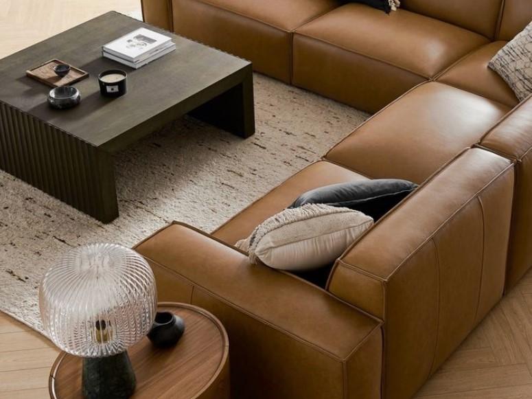 A brown leather couch with pillows and a coffee table